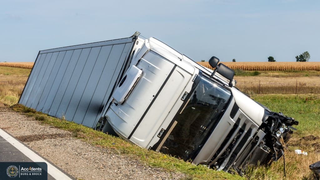 White semi-truck overturned in a grass ditch beside a highway after a rollover crash